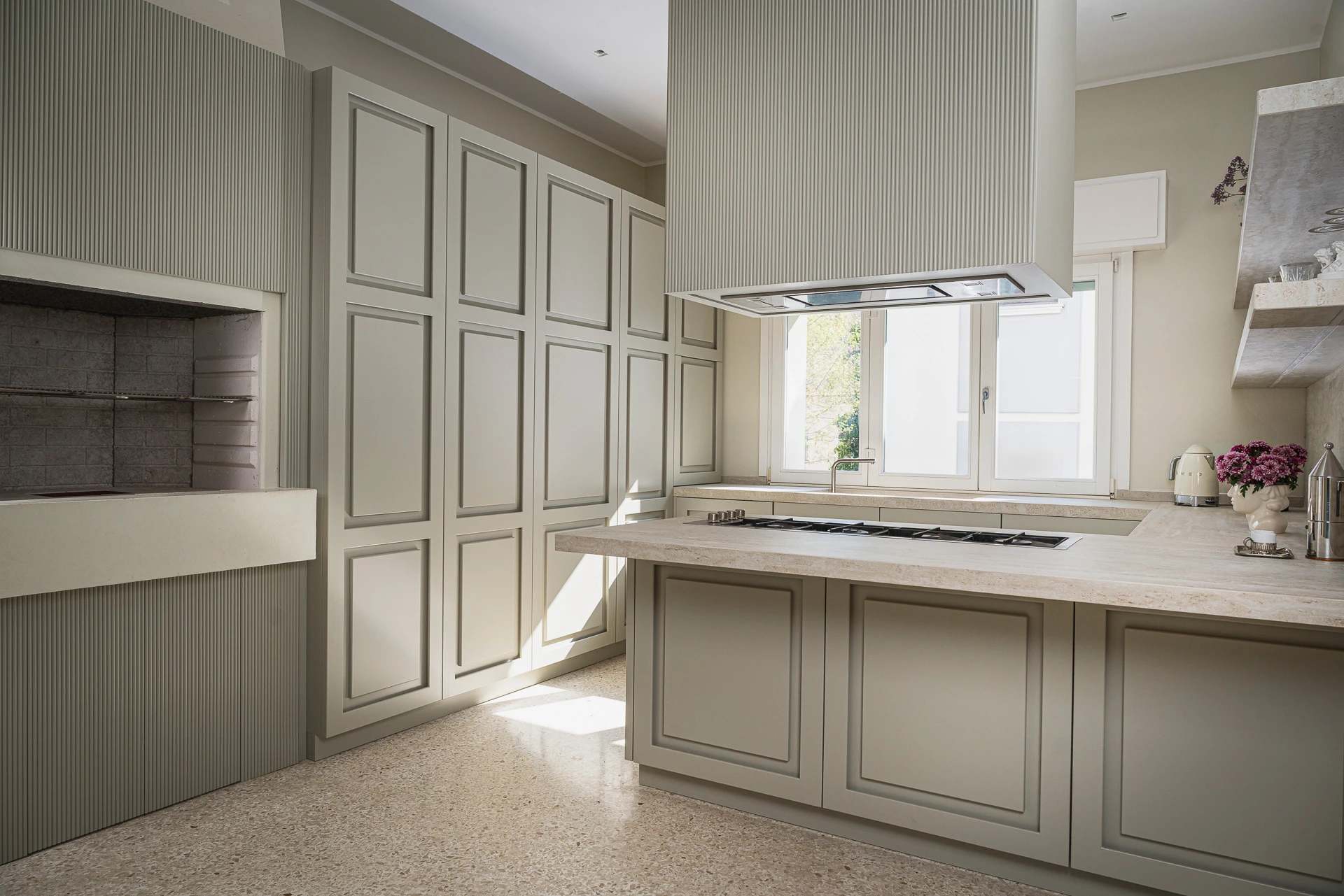 Custom wood kitchen with a floor-to-ceiling pantry, island with gas hob, and suspended fluted hood