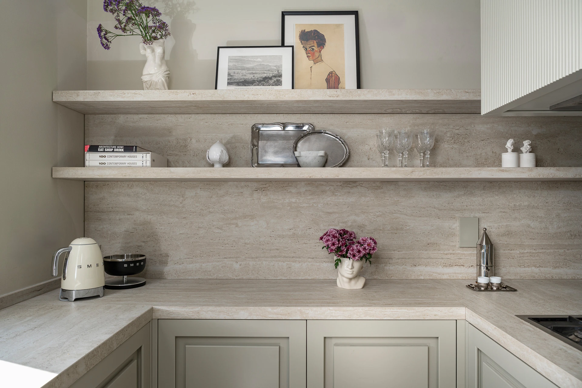 Open travertine shelves integrated into the custom kitchen: glassware, design books, and small Smeg appliances